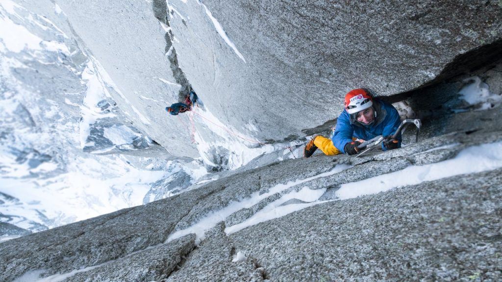 Ueli Steck climbing with ice axe in hand scaling a vertical wall 