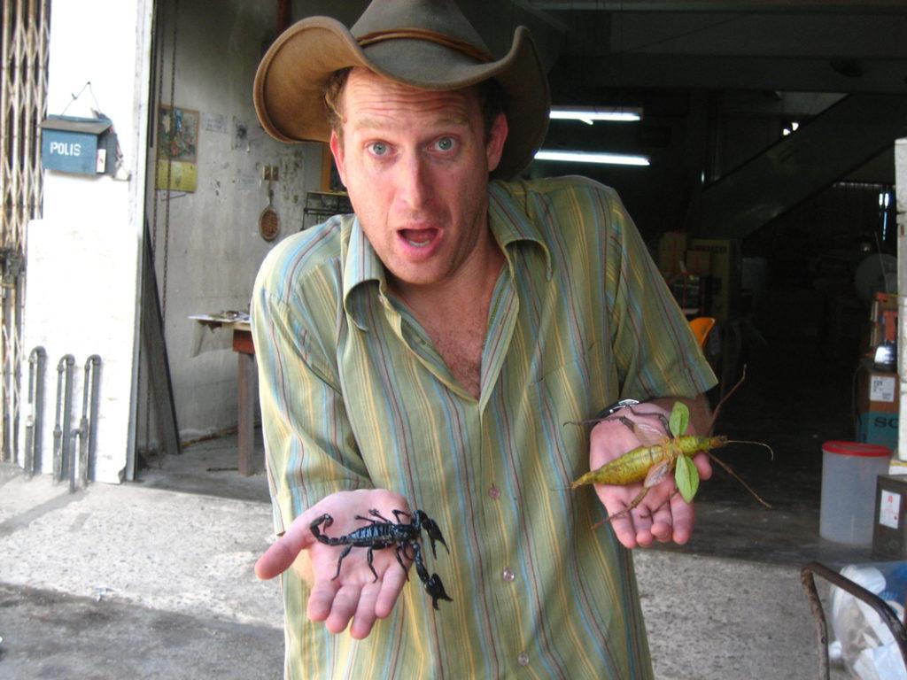 Robin Esrock with a scorpion and leaf bug in Borneo